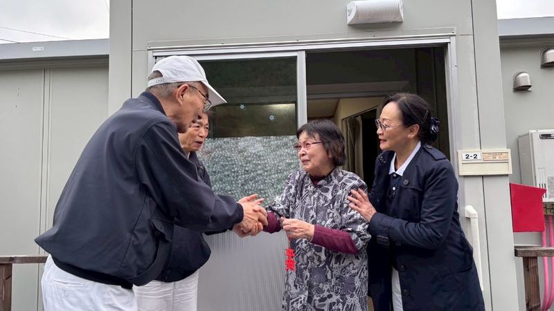 Two Tzu Chi volunteers press a peace charm into the hands of an elderly woman outside temporary housing in Japan.