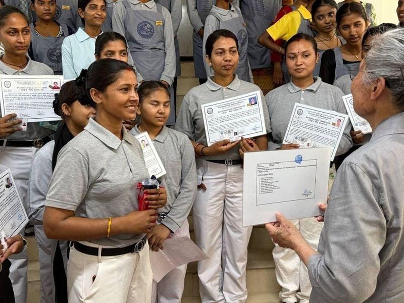 Women in grey training uniforms hold completion certificates after a Tzu Chi vocational sewing course in Nepal.