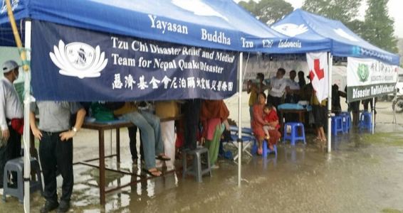 Tzu Chi disaster relief medical tents pitched in the rain after the Nepal earthquake, with staff and patients sheltering beneath them.