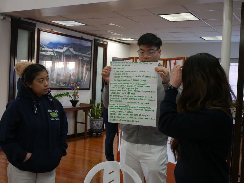 Two students hold up a large handwritten planning poster while a third looks on.